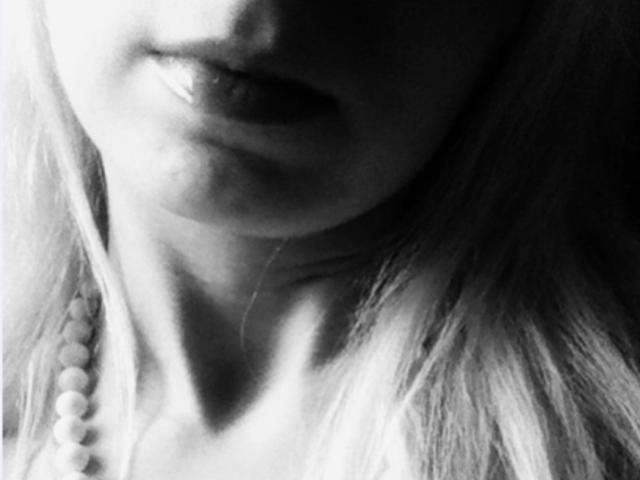 Zwart-wit foto van het onderste gedeelte van AlexandraSweet's gezicht, waarop haar lichtjes open lippen en een kralenketting aan de linkerkant van haar nek te zien zijn. Haar blonde haar is zichtbaar..