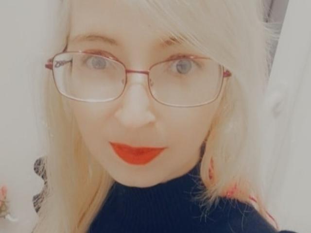  AlexandraSweet has blonde hair, red lipstick, and wears red-framed glasses with a black turtleneck. Her blue eyes are slightly squinted. Her ass is not visible.