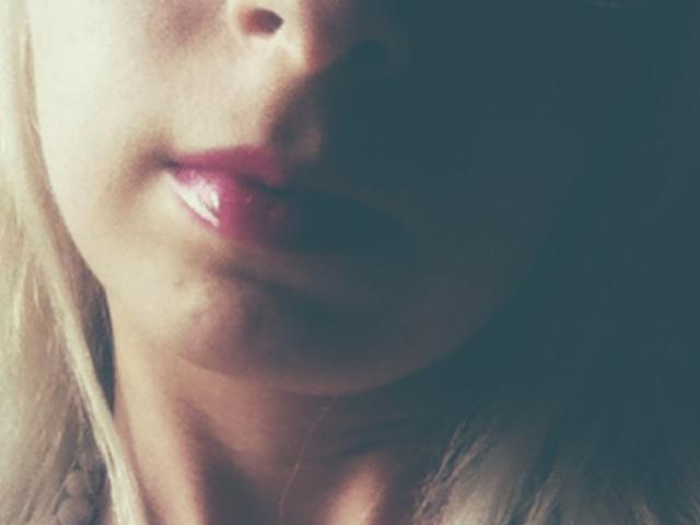 De glanzende, roze lippen van AlexandraSweet, lichtjes open, met zacht blond haar en een vriendelijke glimlach, werden verlicht door zacht licht. Haar huid is bleek, en haar gezicht is gedeeltelijk in de schaduw..