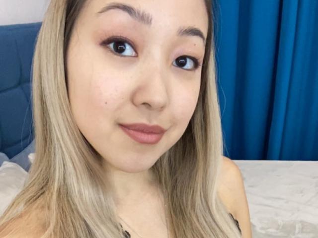 RenyLime has light blonde hair, brown eyes, and pinkish lipstick. She's smiling slightly, showing soft, plump lips and a clear complexion. Her tits are not visible.