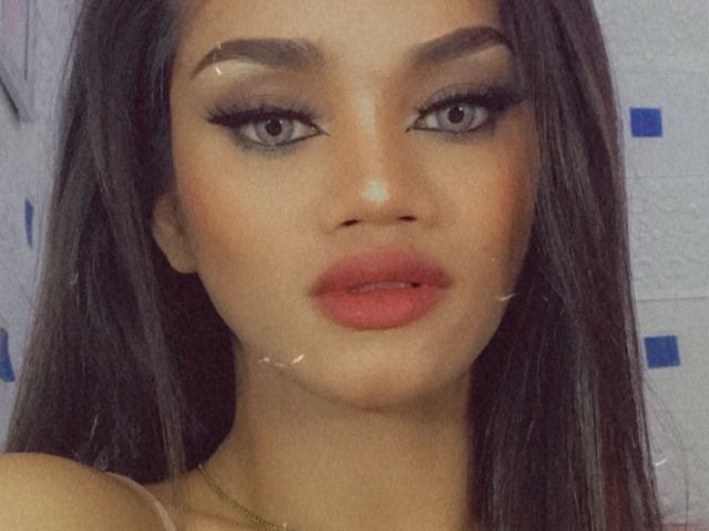SevenInchesCockTS has dark brown hair, thick eyebrows, long eyelashes, and red lips. She has a light skin tone with a small white mark on her chin.