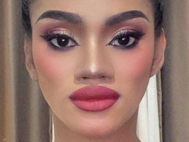 SevenInchesCockTS hat große, dunkle Augen mit dicker Eyeliner, volle, rosa-rote Lippen und einen glatten, strahlenden Teint mit dunklen Augenbrauen. Sie trägt lange, weiße Ohrringe..