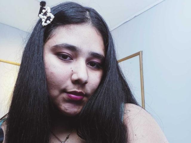 ZoeGiil heeft lang zwart haar, paarse lippenstift en een klein sproetje op haar neus. Ze draagt een witte haarspeld en een zwarte ketting op deze selfie..