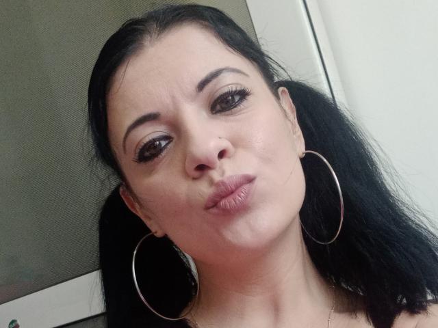 AdriannaLily with puffy lips, dark brown eyes, black hair in pigtails, wearing large hoop earrings, slightly smushed nose, and a small nose ring, looking at the camera.