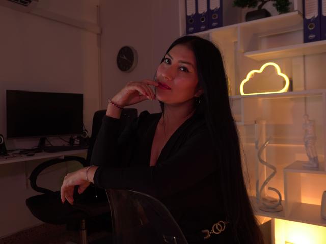 KatyaScott, long black hair, dark top, cute, smiling, hand on chin, black chair, office, neon cloud light, dark room, subtle makeup, pink lips, relaxed, sexy.