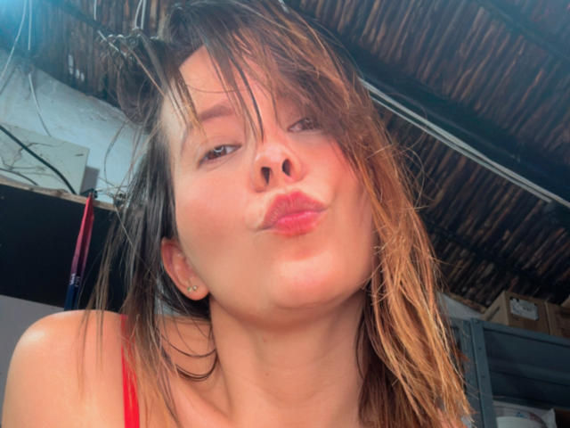SaritaVelez has puffy pink lips, slightly messy brown hair, and a red top, making a goofy pouty face with a small nose ring visible on her left ear.