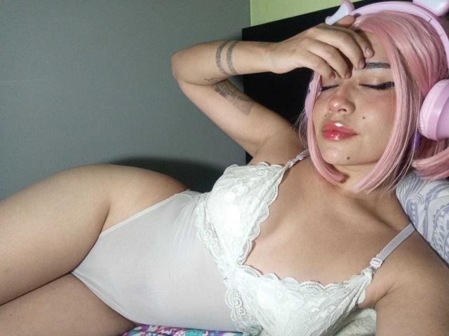 AnniEvans with pink bob and headphones, sleeping in white lace bodysuit, showing her tits and ass, hand on forehead, tattoo on arm, pink lips, soft lighting, relaxed.