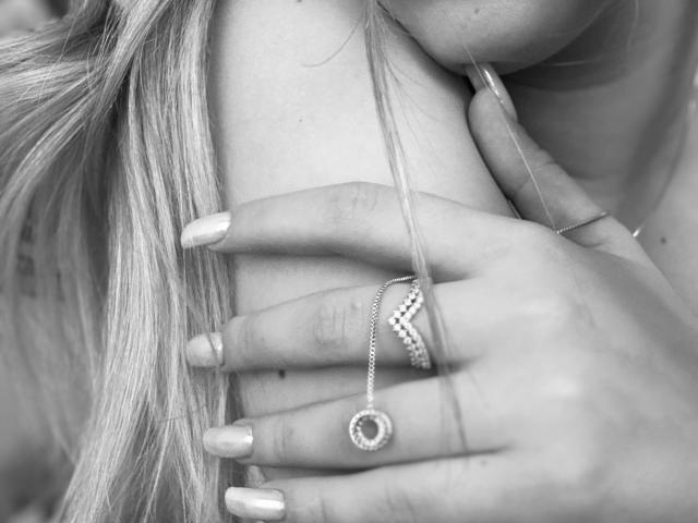 Las manos de SugarrX, con uñas largas y anillos, uno de ellos con una gema circular, acariciaban suavemente sus pechos, mientras su cabello rubio caía sobre su pecho. Foto en blanco y negro..