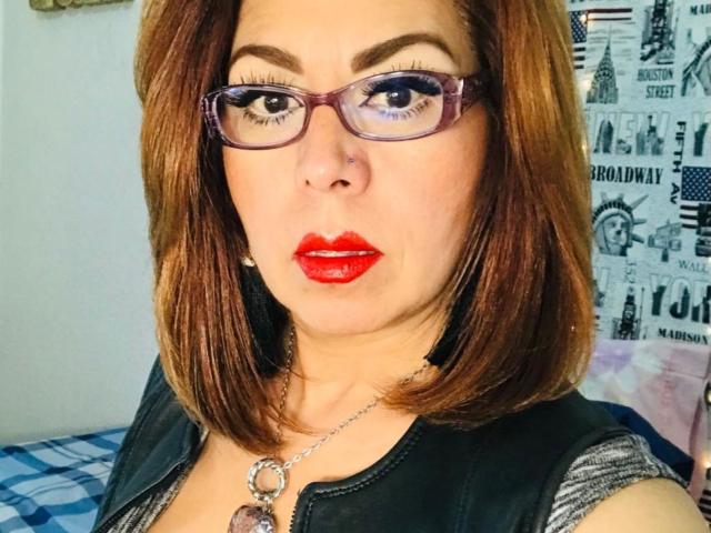 CatherineMilf has red lipstick, glasses, and brown shoulder-length hair, wearing a black top with a silver necklace, showing her nose ring and red lips, with her tits partially visible.