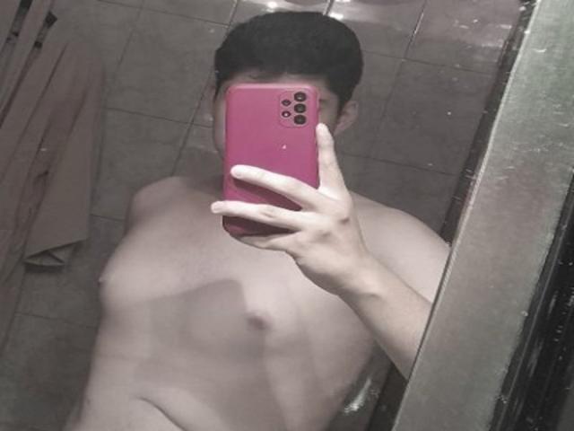 Naked SexyBoyRogerz with short dark hair, holding a pink phone, covering his face, taking a mirror selfie, showing a slim, pale chest with small nipples.