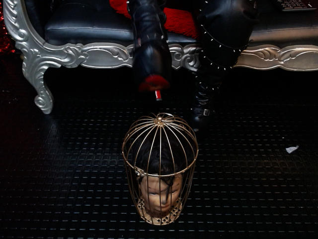 SamyWalker's black boot with a red sole is dripping red liquid onto a metal birdcage with a face, sitting on a black textured floor.