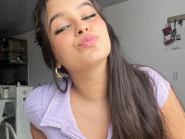 Kaary69 with pouty pink lips, long brown hair, wearing a purple ribbed shirt, gold hoop earrings, and heavy eyelashes, slightly tilted head, eyes closed, soft pink blush on cheeks.
