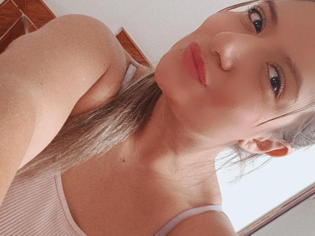 ValeriaHunter69, con labbra rosa carnose, occhi marroni e capelli castani lisci, indossa una canottiera bianca a coste che mette in mostra le spalle e il petto. Il suo seno piccolo è leggermente visibile..