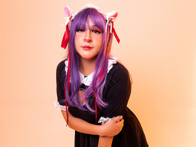 KittyEla with purple hair, cat ears, and black maid outfit, leaning forward with arms crossed, looking cute with red ribbon accents and white lace on her dress.
