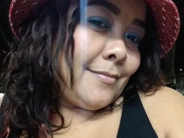 SussanHott has curly brown hair, a nose ring, blue eyeshadow, and a slight smirk, wearing a red patterned bucket hat and a black tank top.