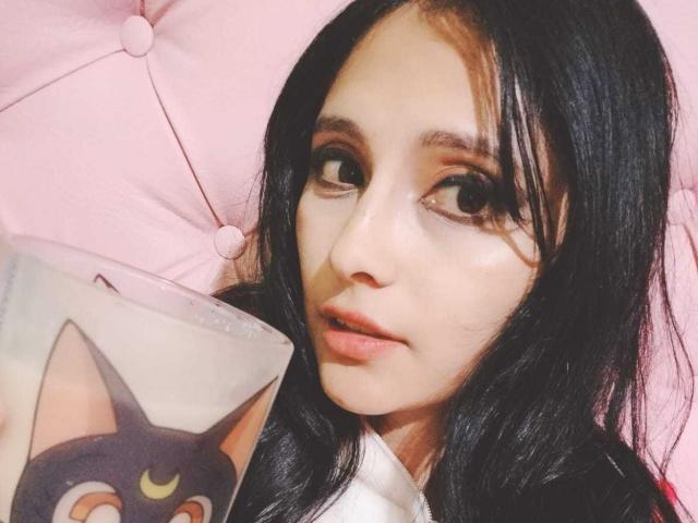 MidoriChang with long black hair, brown eyes, and light skin, holding a book with a cat face, pink tufted background, and soft light. Boobs not visible, pussy not visible.