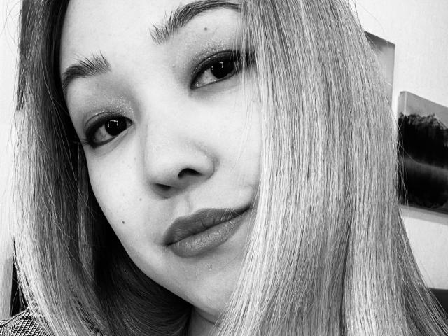 Black-and-white selfie of RenyLime with straight, medium-length hair, slightly raised eyebrows, dark eyeliner, and subtle lipstick, showing a gentle, confident smile. RenyLime's nose is centered.