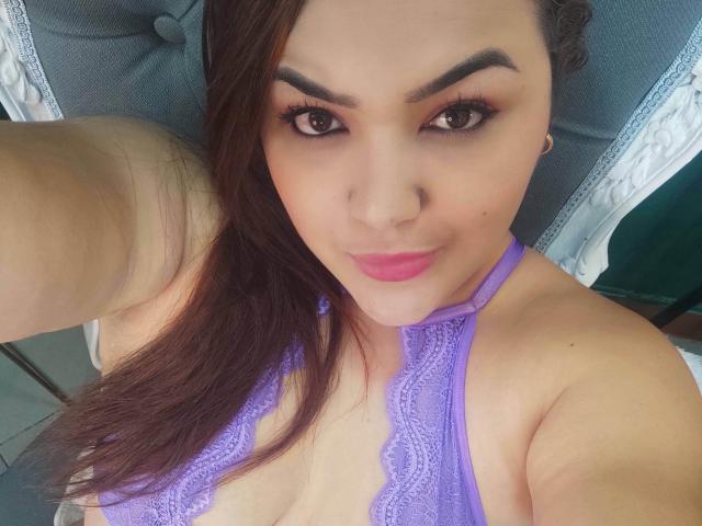 RouseWatsons with purple lace top, brown eyes, pink lipstick, and long brown hair, showing tits in selfie, smiling at camera.