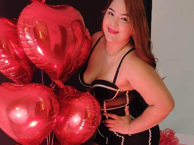 RouseWatsons mit roten, herzförmigen Ballons, trägt ein schwarzes Kleid mit weißen Trägern, eine goldene Kette und roten Lippenstift, lächelt in die Kamera und zeigt ihre Brüste..