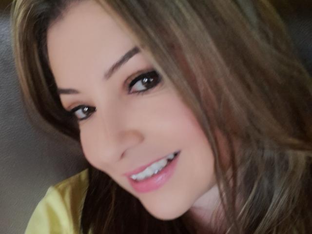 NatalyHami has brown hair, dark eyes with black eyeliner, and a pink smile showing white teeth. She's looking slightly up and to the left with a cute, soft smile.