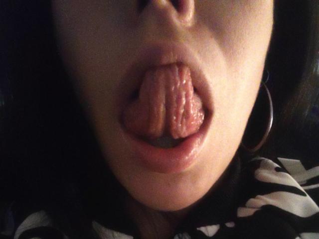 SeleneBright's face with her tongue out, wet and glistening, covering her pink, slightly parted lips. She's wearing hoop earrings and a black-and-white striped shirt.