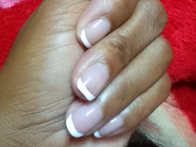 La mano de Maryssah, con uñas rosadas brillantes y puntas blancas al estilo francés, y piel marrón oscura, juntando los dedos, mostrando sus zapatos de baile impecables y bien cuidados..