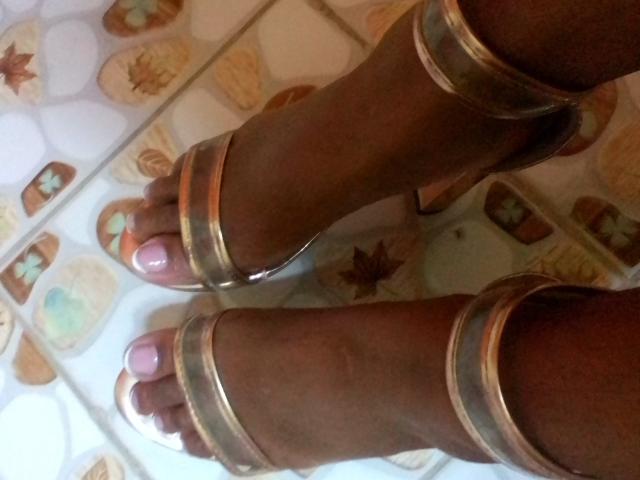 Maryssah's dark brown toes with pink nail polish, wearing gold metallic sandals, are in the frame. Her feet are slightly apart on a patterned surface.
