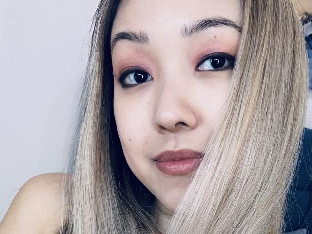 RenyLime has blonde hair, light skin, and pink eyeshadow. Her brown eyes look slightly to the side with a subtle smile on her pink lips.