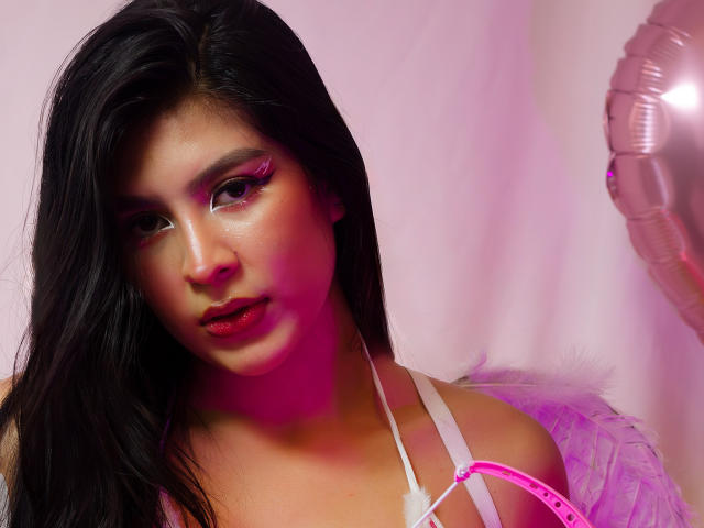 SamanthaEva69 heeft lang zwart haar, roze eyeliner en glanzende roze lippen. Ze draagt een roze bandje en witte veren, met roze verlichting op haar gezicht. Borsten zichtbaar..