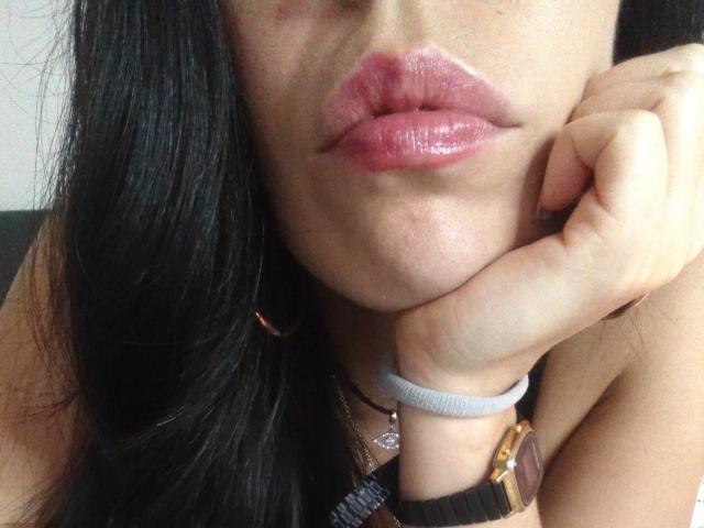 SeleneBrigth's puffy pink lips with glossy lipstick, black hair, and a hand resting on her cheek, wearing a gold watch and a white wristband.