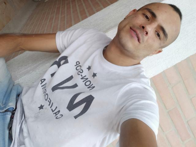 StrongAlan, short-cropped, light-skinned, wearing a white t-shirt with black text, slightly smiling, sitting with arms relaxed, blue jeans, overhead selfie, bald, casual, relaxed, confident.