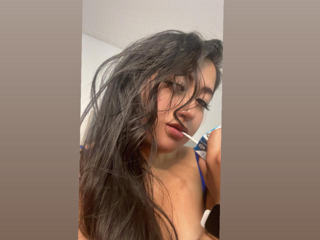 ShannelTaylor with messy dark hair, blue strap lingerie, and a white toothbrush in her mouth, looking slightly down. Boobs visible, nipples not shown. Soft lighting, casual selfie.
