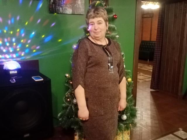 LeeNell, short gray-haired woman, wearing brown sparkly dress, standing by Christmas tree with lights, next to black speaker with colorful light reflection, smiling slightly, small tits, average ass.