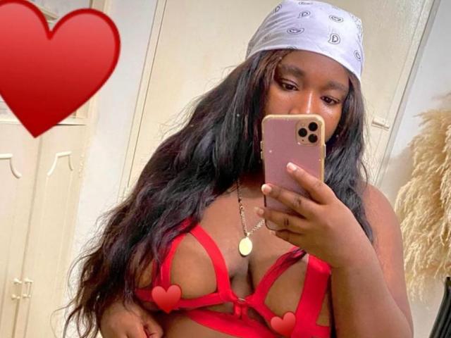 NahirobyEbony with dark skin, long black hair, wearing a white bandana, red strappy lingerie, heart emojis covering her tits, taking a mirror selfie with a pink iPhone.