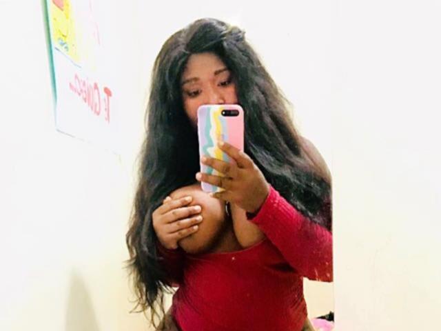 NahirobyEbony with long black hair, red long-sleeve top, holding her big tits with one hand, taking a mirror selfie with a colorful phone case.