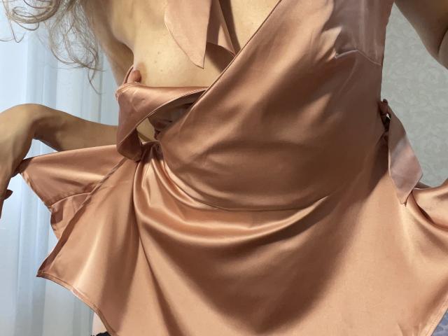 TheHottestBlonde's pink satin dress, partially pulled down, reveals a hint of her small, perky tits and a sliver of her flat, pale-ass. Soft, shiny fabric, subtle shadows.