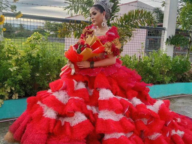 MajesticTrannyCock in a huge red and white ruffled dress, holding a bouquet, wearing a sparkly crown and red gloves, with large white earrings, and dark makeup.