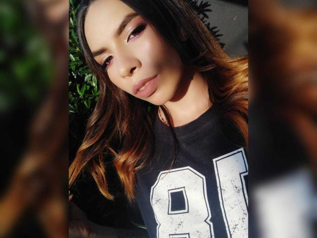 VioletaStone a les cheveux bruns ondulés, un fard à paupières rose et une bouche légèrement entrouverte. Elle porte un t-shirt noir avec l'inscription "81" et regarde vers le bas avec une expression douce et confiante..