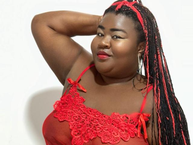 BritannyJhonson with dark skin, red lace top, and long black-red braids, hand in hair, smiling, red lipstick, earrings, white background, confident, sexy.