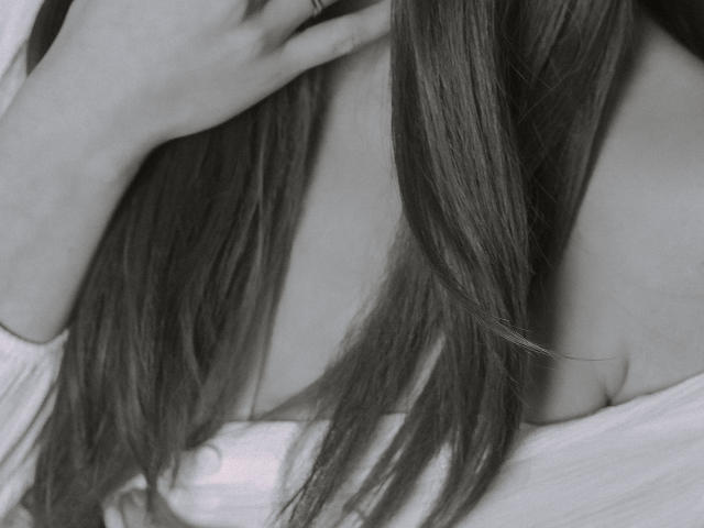 JaneRoller's long, straight hair covers her bare shoulders and upper chest, with her hand gently touching her neck. She's wearing an off-shoulder white top. Black-and-white photo.