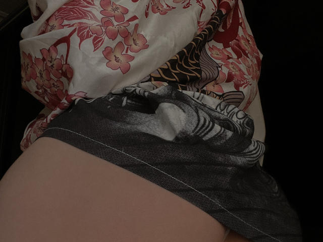 JaneRoller's ass, wrapped in a floral and zebra-print fabric, with a gray, black, and white patterned bottom pulled down, exposing her pale, smooth skin. Dark background.