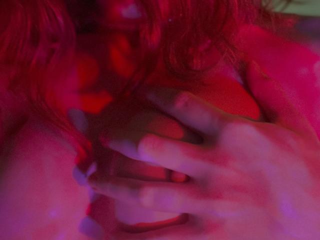 JaneRoller's hands are gently covering her tits under a red and pink light. Her fingers are slightly curled, with a soft, sensual glow.