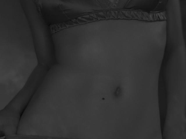 JaneRoller's bare, dark-skinned belly with a small, black mole just below her navel, wearing a satin bra, shot in grayscale.