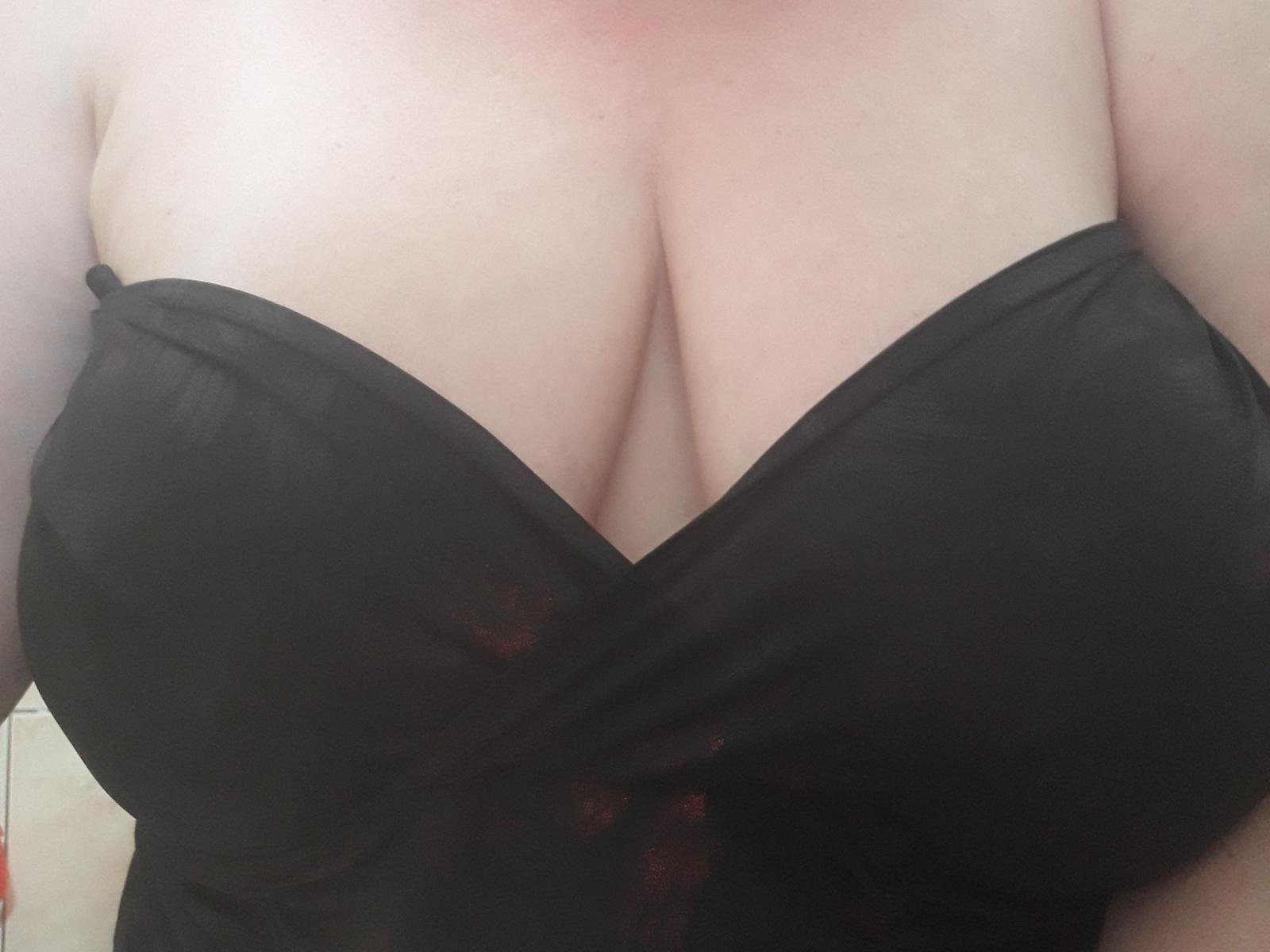 LoveMilfX's big, round boobs are covered in a black, strapless top that's crisscrossing over her cleavage. Her pale skin is visible above the top.