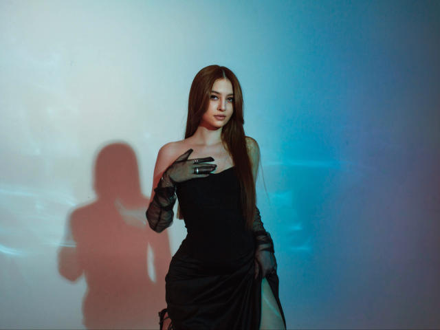 EllyCat with long brown hair, black strapless dress, and black gloves, touching her chest, shadow on wall, blue and white light, looking at camera, sultry expression, sexy.