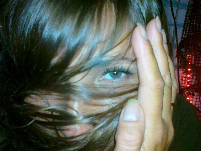 Ellita's blue eye peeks through her messy brown hair as she uses her right hand to cover part of her face. Her fingers are slightly bent, showing her nails.