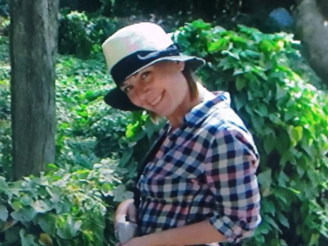 Diana, sorridente, indossa una camicia a quadri e un cappello nero con una tesa bianca, ed è in piedi in una zona verde e alberata, mostrando leggermente il seno nella foto..
