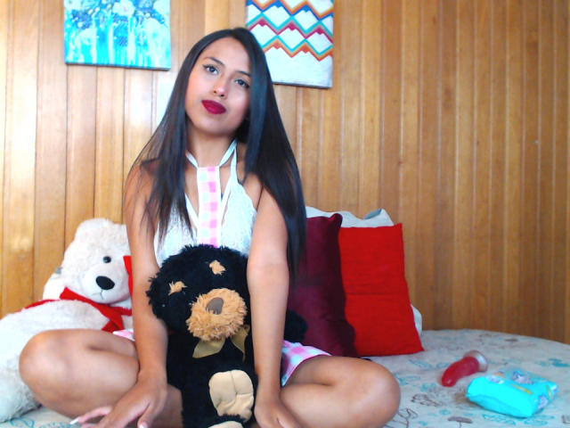 MyaaTyler is in front of a wall of large, 3D, royal blue and red flags. Flags have bold, black lettering and symbols. Flags are evenly spaced, overlapping slightly.