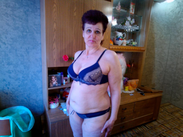 PaulaGoldens, middle-aged with short dark brown hair, wearing dark blue lace bra and matching panties, standing in a room, showing her tits and slightly sagging ass, looking at camera.