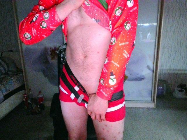 Svit, wearing red Christmas pajamas with snowmen, has their shirt lifted to show a hairy, pale chest and unbuttoned red shorts, exposing a flaccid, uncircumcised, slightly red, small cock.